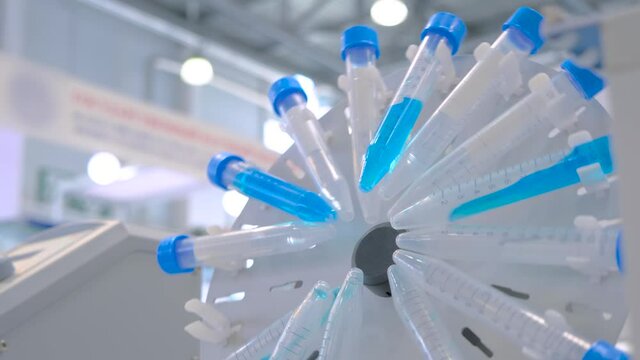 Slow motion: digital circular tube rotator for effective mixing biological blue samples at pharmacy factory, medical exhibition: close up. Chemistry, pharmaceutical, laboratory equipment concept