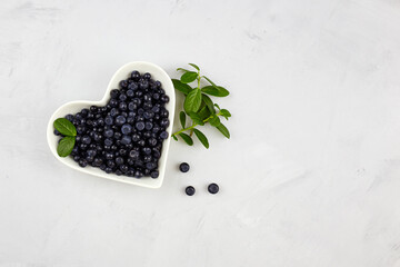 Blueberries in bowl in the shape of a heart on a light background