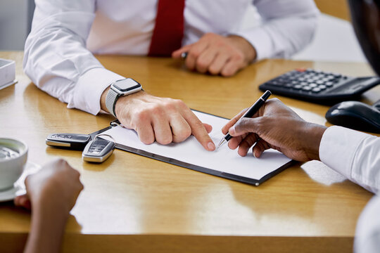 helpful manager of dealership gives necessary information and instruction to clients, explains everything before signing a contract. close-up photo of hands and documents