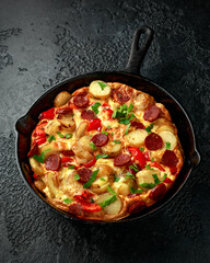 Frittata made of eggs, potato, chorizo, red bell pepper and greens in iron cast pan