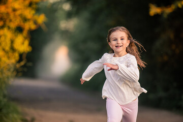 girl junior schoolgirl runs along the road in the evening in the park, happy face, bright emotions,...