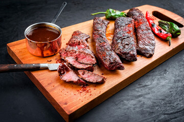 Barbecue wagyu skirt beef steak with hot chili and spice BBQ sauce offered as close-up on wooden design board