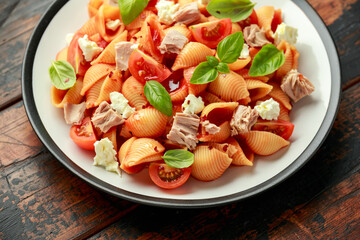 Conchiglie Tuna pasta with tomato sauce, feta cheese and basil on wooden table.
