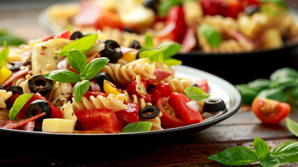 Antipasto salad with pasta, tomato, olives, red onion, bell pepper, salami, cheese, artichoke and basil.