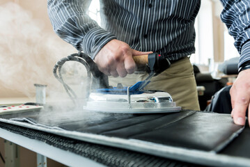 Designer tailor sew seat covers. Man use iron for his work.