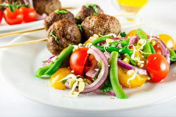 Lula kebab from lamb on a wooden skewer with a salad from Cherry tomatoes, red onions and green beans. White background. Selective focus.