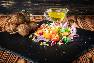 Lula kebab from lamb on a wooden skewer with a salad from Cherry tomatoes, red onions and green beans. Slate plate on a wooden background. Selective focus.