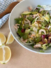 Salad with shrimp, avocado, lemon and arugula. On a wooden table with a tea towel and a wooden spoon