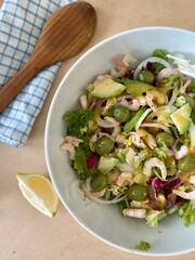 Salad with shrimp, avocado, lemon and arugula. On a wooden table with a tea towel and a wooden spoon