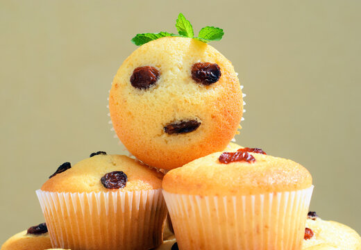 Freshly baked homemade muffins, some with funny faces. Vanilla muffins with raisins, decorated with melissa leaves