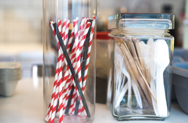 Eco recycling paper straws for drinks, wooden tea and coffee sticks, plastic spoons, knives and forks in a glass jar at the cafe restaurant