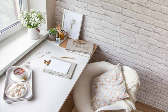 Work Table Near The Window In The Scandinavian Nordic Style. Female Work And Home Office Concept. White And Gold Office. Flowers In A Vase And Rings, Bracelets On The Table.