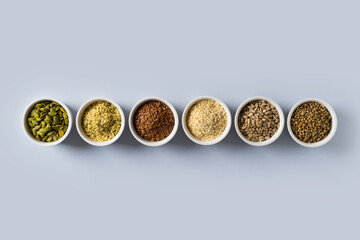 Different seeds - hemp, sesame, sunflowers seeds and pumpkin seeds in small bowl top view on blue background