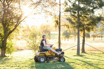 Young boy riding ride on lawn mower in golden afternoon light