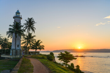 Fototapeta na wymiar phare blanc entouré de palmier devant une mère superbe au sud de l'ile du Sri Lanka