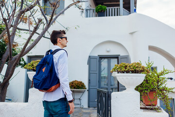 Man traveler walking in village looking at architecture on Santorini island, Greece. Tourist backpacker renting house