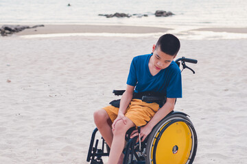 Asian special child on wheelchair smiling happily on the beach,Seaside nature background with day light, Life in the education age of disabled children, Boy have outdoor activities like normal people.