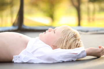Blonde hair blue eyed boy lying on trampoline with white shirt undone