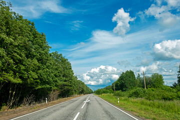 Asphalt road among the trees and blue sky with clouds