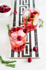 Cold  fresh summer berry lemonade with rosemary,raspberry and ice in glasses on a light background