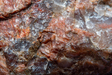 Photograph of a granite surface interspersed with transparent mica in soft focus at high magnification. Fine texture of natural mineral of pink color with blurred background.