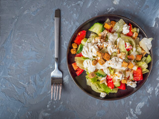 Light breakfast with caesar salad on a black plate and a table fork on a gray background