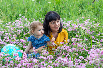 young mother with little daughter on a flower meadow in a park on a summer day