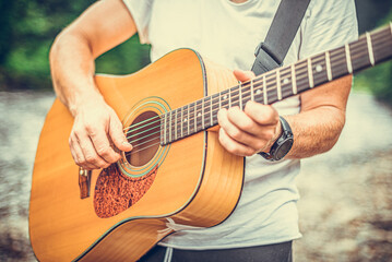 Fototapeta premium Acoustic Guitar Playing. A man plays the guitar against the background of nature.