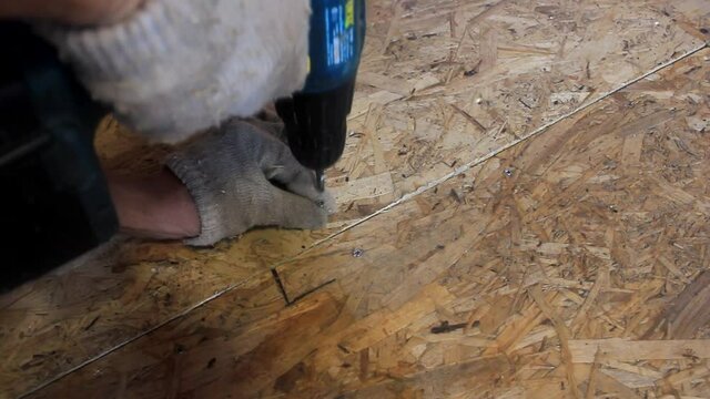 Driving screws into the floor (osb) with a screwdriver. Man's hands