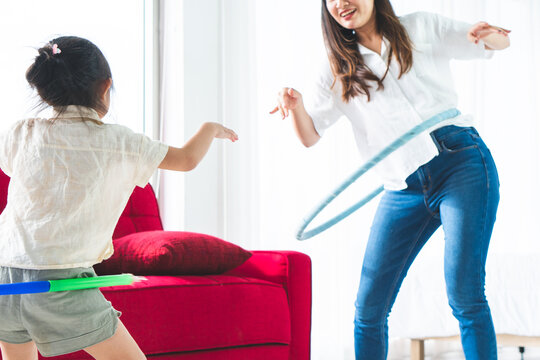 Young Asian Girl Playing Hula Hoop With Her Mother In The Living Room In The Summer Time. Family Relationship And Together Concept