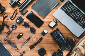 Top view with a digital camera, charger, camera, lens, video camera, USB, personal laptop, book, pen, glasses, remote control, and electronics camera accessory photography concept on wooden background