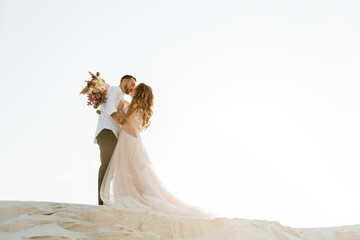 Love Story of a beautiful couple in a pink wedding luxury dress with a bouquet in the Sahara...
