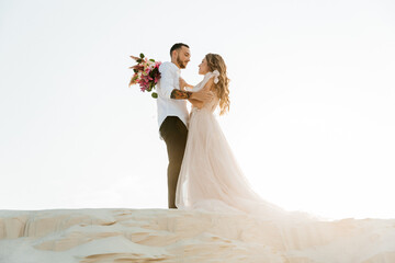 Love Story of a beautiful couple in a pink wedding luxury dress with a bouquet in the Sahara desert, sand, dunes