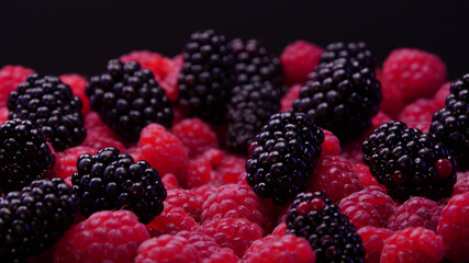 Close up of blackberries and raspberries fruits on plate and a black background. Fresh and tasty looking organic food for vegan in a summer season. Forest fruits.