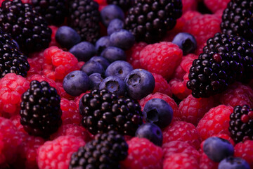 Fresh berries composition. Raspberries, blackberries and blueberries on black background. Tasty looking organic fruits covered with dew.