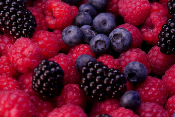 Fresh berries composition. Raspberries, blackberries and blueberries on black background. Tasty looking organic fruits covered with dew.