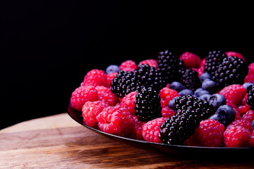 Fresh berries composition. Raspberries, blackberries and blueberries on black background. Tasty looking organic fruits covered with dew.