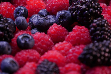 Fresh berries composition table top. Raspberries, blackberries and blueberries on black background. Tasty looking organic fruits covered with dew.