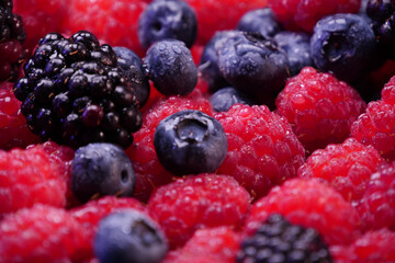 Fresh berries composition. Raspberries, blackberries and blueberries on black background. Tasty looking organic fruits covered with dew.