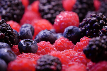 Fresh berries composition. Raspberries, blackberries and blueberries on black background. Tasty looking organic fruits covered with dew.