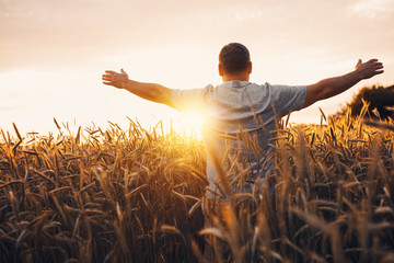 Sunrise or sunset picture of guy with raised hands looking at sun and enjoying daytime. Adult man...