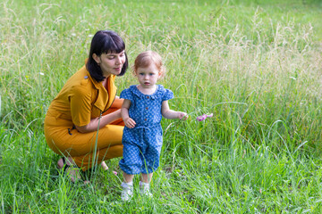 a young mother with a little daughter with a pink flower in her hand on a meadow with green grass in a Park on a summer day