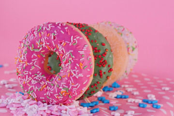 Four nicely decorated, tasty looking various color donuts with colorful sprinkles. Beautiful pink wallpaper with sweet and delicious doughnuts.	