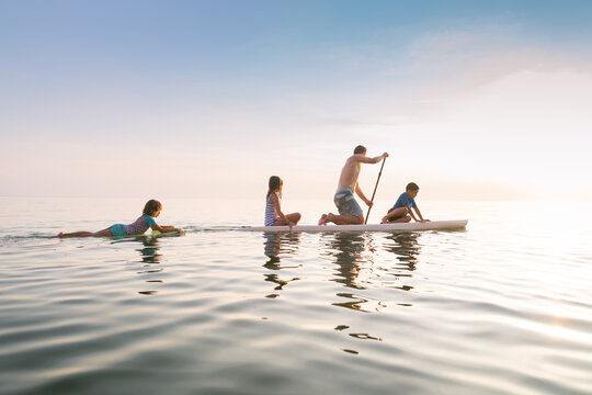 Father and children on paddle board at sunset on lake michigan
