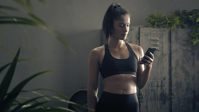 woman using smart phone with personal trainer workout app at home. Woman preparing for workout using fitness app. Close orbit shot.Woman using mobile phone while resting during fitness training 