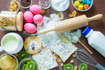 Baking background with organic eggs, flour, wheat grains, oatmeals, butter, raisins and rolling pin on dark wooden table. Pastry making and bakery concept, top view, copy space