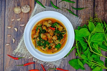 Stir fried spicy crispy pork belly with Thai basil surrounded with key ingredients on wooden table. Authentic Thai food.