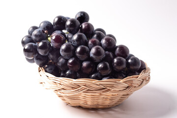 Black grapes without seeds in a rattan basket. White background