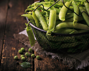 Pods of young green peas in a wooden bowl on the table