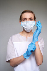 Close up of female doctor or scientist in protective medical mask over grey background. She is puting on gloves